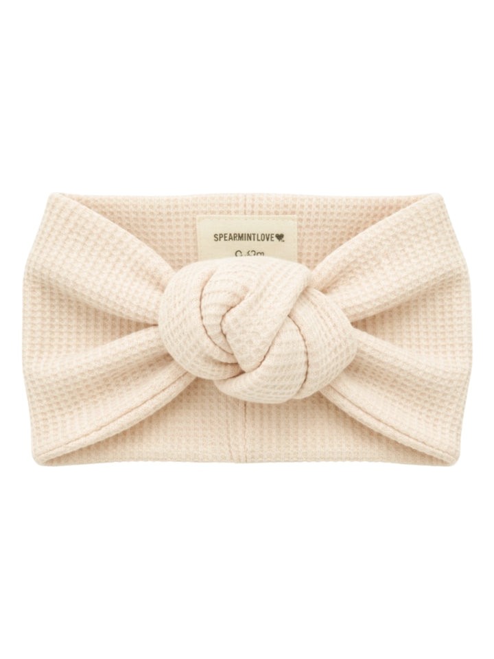 Cream-colored knotted headband made of textured fabric, labeled 'SPEARMINTLOVE.'