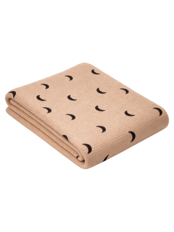 Tan blanket with black crescent moon patterns, folded neatly on a white background.