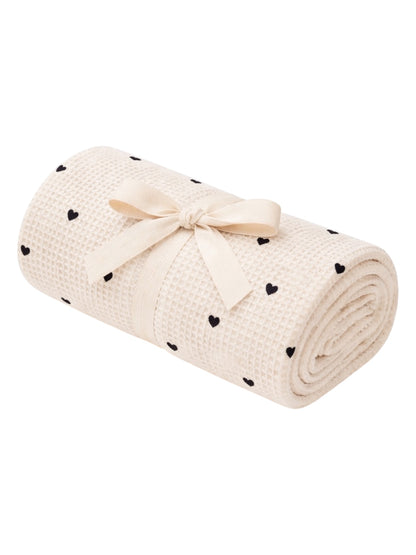 Rolled cream blanket with black heart patterns, tied with a ribbon, ideal for cozy settings and decorative use.