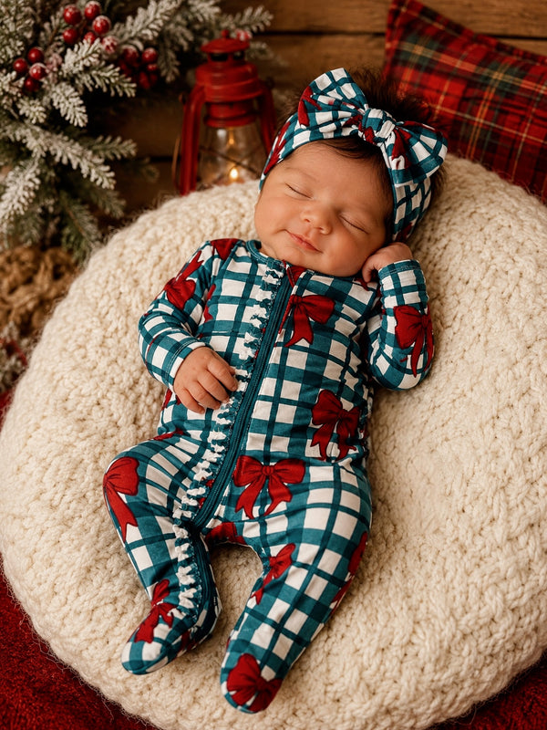 Baby in a festive outfit with red bows, resting on a cozy blanket, against a warm holiday backdrop.