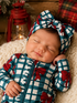Smiling baby in a blue and white plaid outfit with red bows, peacefully sleeping on a cozy blanket.