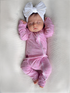 Sleeping baby girl in pink onesie with white bow headband, resting on a textured blanket.