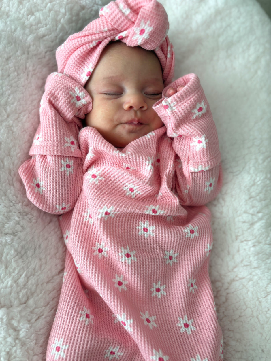 Baby girl smiling in a pink floral outfit with a matching headband, resting on a soft blanket.