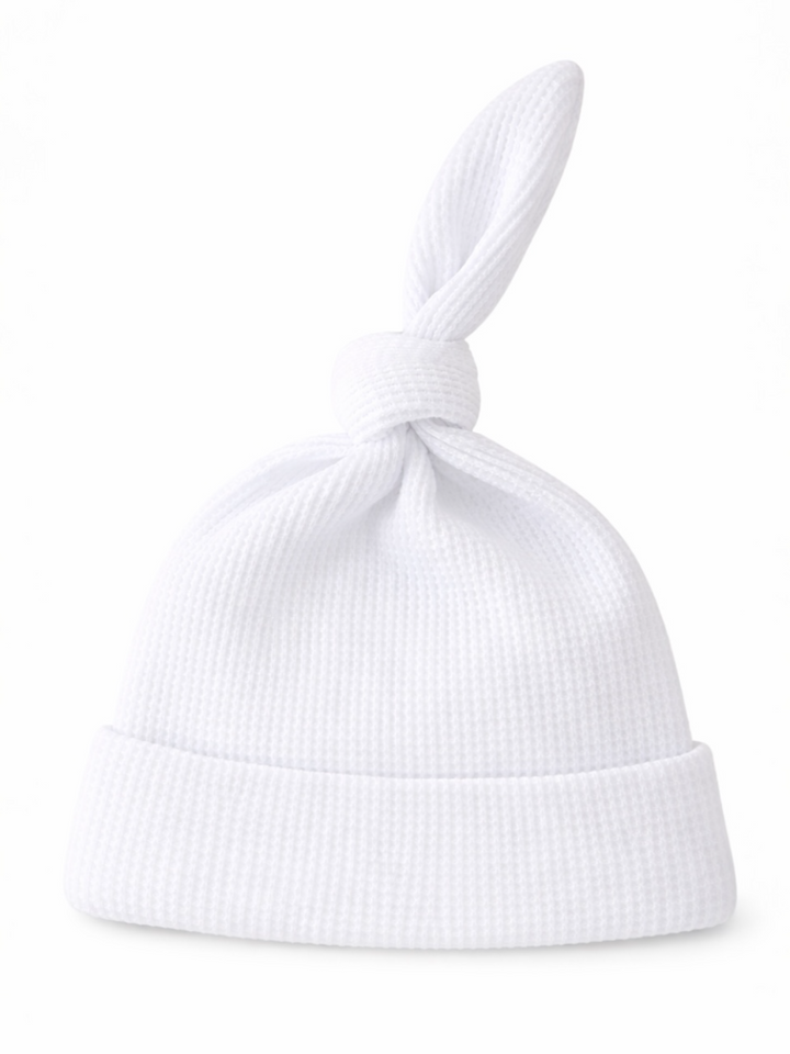 White baby hat with a knot at the top and a folded brim, made from textured fabric.