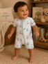 Smiling toddler in a bear-patterned onesie stands in a cozy room with toys and decor.