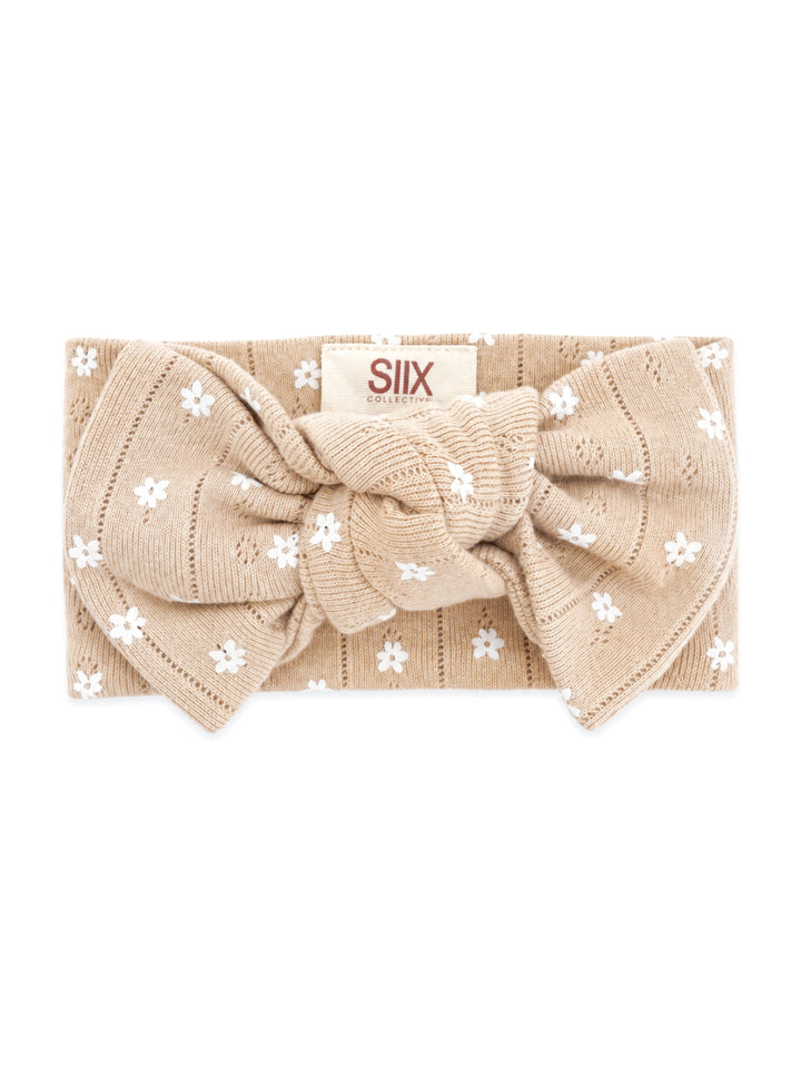 Beige headband with white floral patterns and a large bow, labeled "SIIX COLLECTIVE."