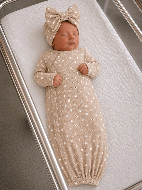 Baby doll wearing a floral-patterned gown and a matching bow headband, resting in a crib.