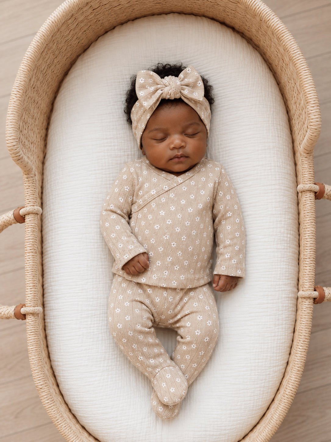 Infant sleeping in a cozy bassinet, wearing a beige outfit with floral patterns and a matching headband.