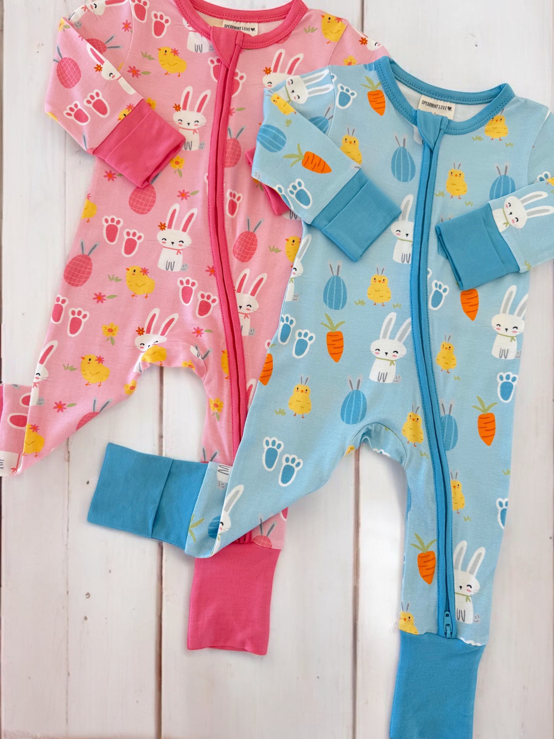 Two colorful children's pajamas, one pink with bunnies and chicks, the other blue with carrots and cute animals.