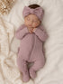 Newborn baby girl in a purple outfit with a bow, sleeping on a cozy white blanket.