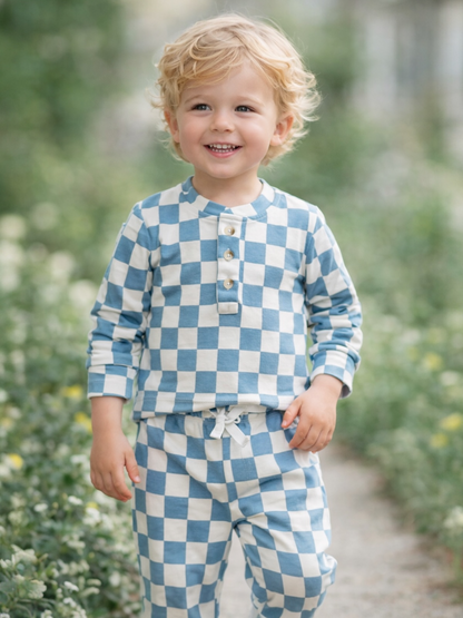 Smiling child wearing blue and white checkered pajamas, walking through a garden path.