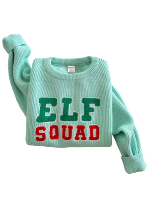 Mint green sweater with "ELF SQUAD" text in red and green letters, folded on a white background.