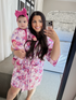 Mother and baby, both in floral outfits, smile for a mirror selfie in a bright, modern room.