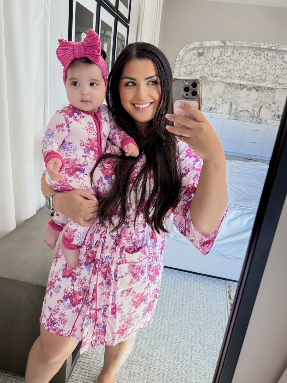 Mother and baby, both in floral outfits, smile for a mirror selfie in a bright, modern room.
