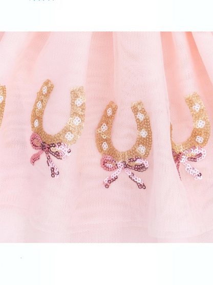 Pink tulle fabric decorated with golden sequined horseshoes and bows. Ideal for festive clothing or accessories.