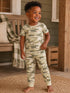 Smiling toddler in camouflage pajamas stands on a porch, showcasing a joyful expression.