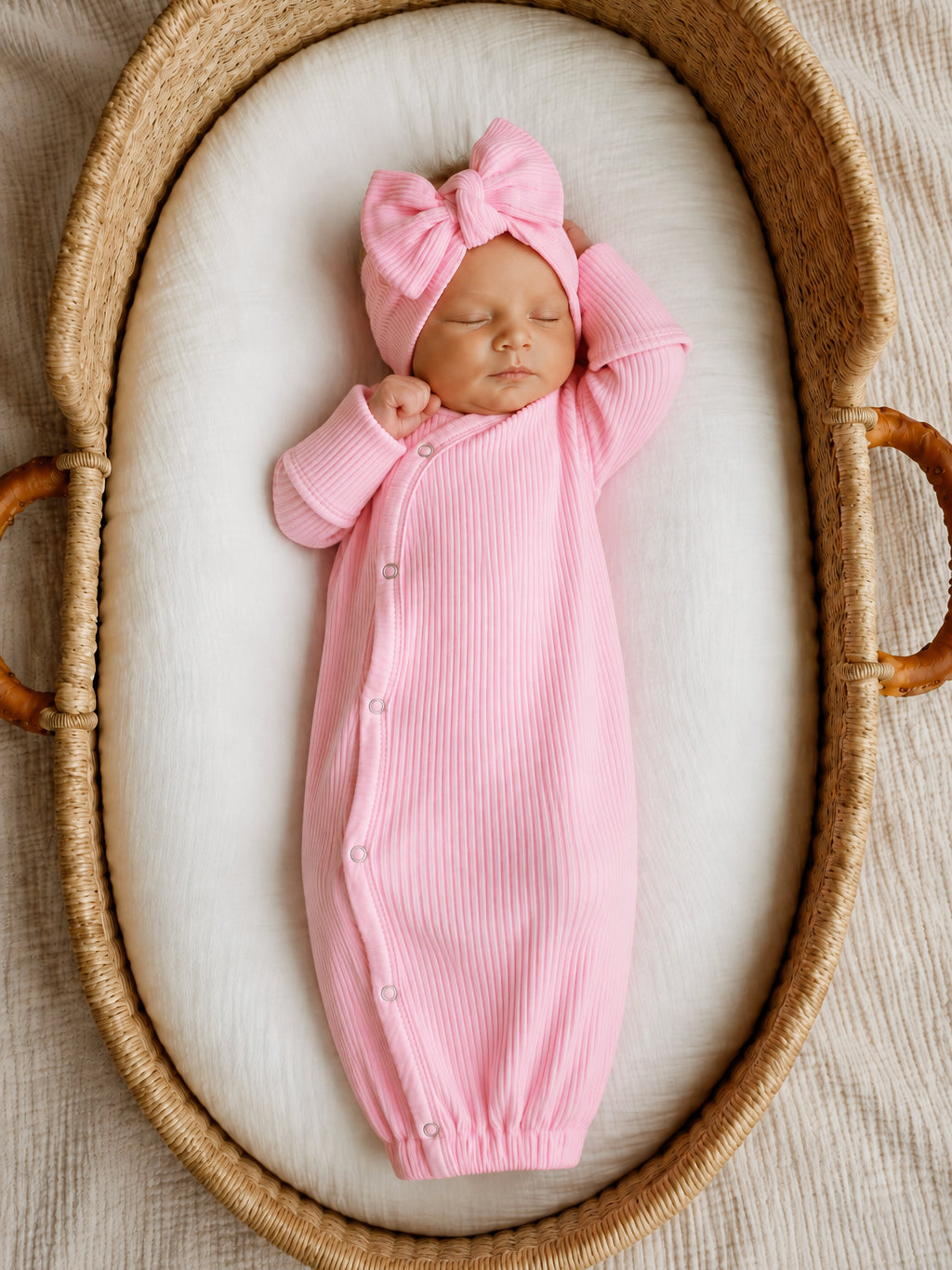 Newborn baby girl in a pink ribbed outfit and bow, peacefully sleeping in a cozy woven basket.