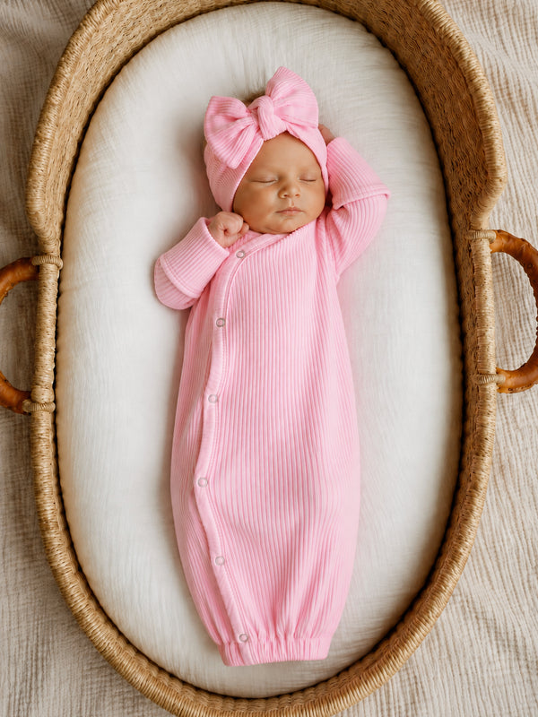 Newborn baby girl in a pink ribbed outfit and bow, peacefully sleeping in a cozy woven basket.