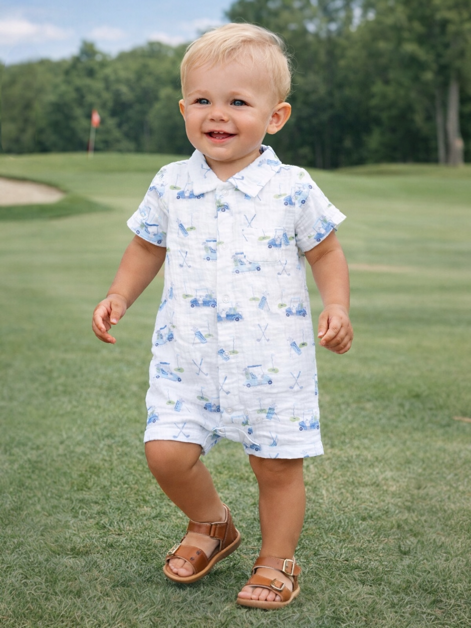 Smiling toddler in a playful golf-themed romper, walking on grass at a golf course.
