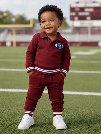 Smiling toddler in maroon outfit stands on a football field, wearing white sneakers and an MVP patch.