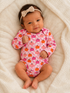 Smiling baby in a pink pumpkin-patterned onesie, laying on a soft, cream-colored blanket.