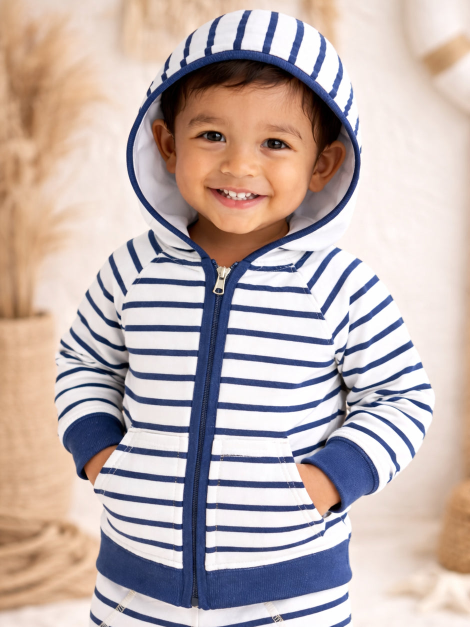 Smiling child in a striped hoodie with a hood, standing in a soft, neutral background.