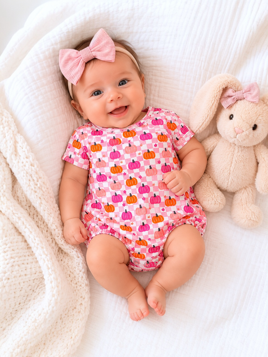 Smiling baby in a colorful pumpkin outfit, lying on a blanket with a soft bunny toy.