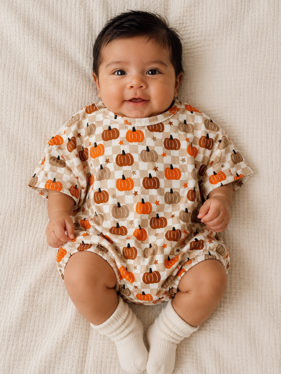Smiling baby wearing pumpkin-themed outfit, sitting on a textured blanket. Soft lighting highlights their joyful expression.