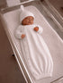 Newborn baby sleeping in a white ribbed gown and hat in a hospital bassinet.