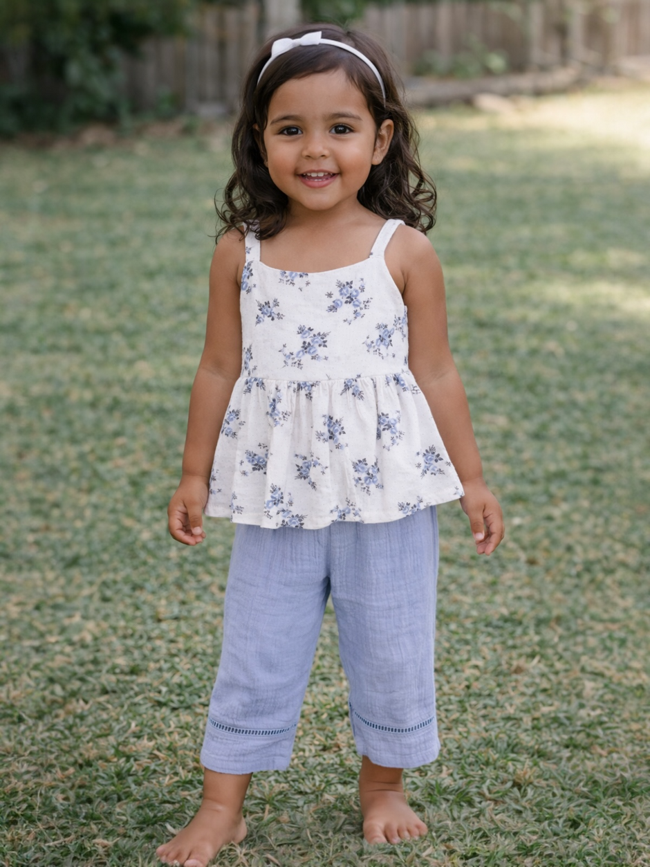 Smiling young girl in floral top and blue pants standing on grassy lawn. Bright and sunny outdoor setting.