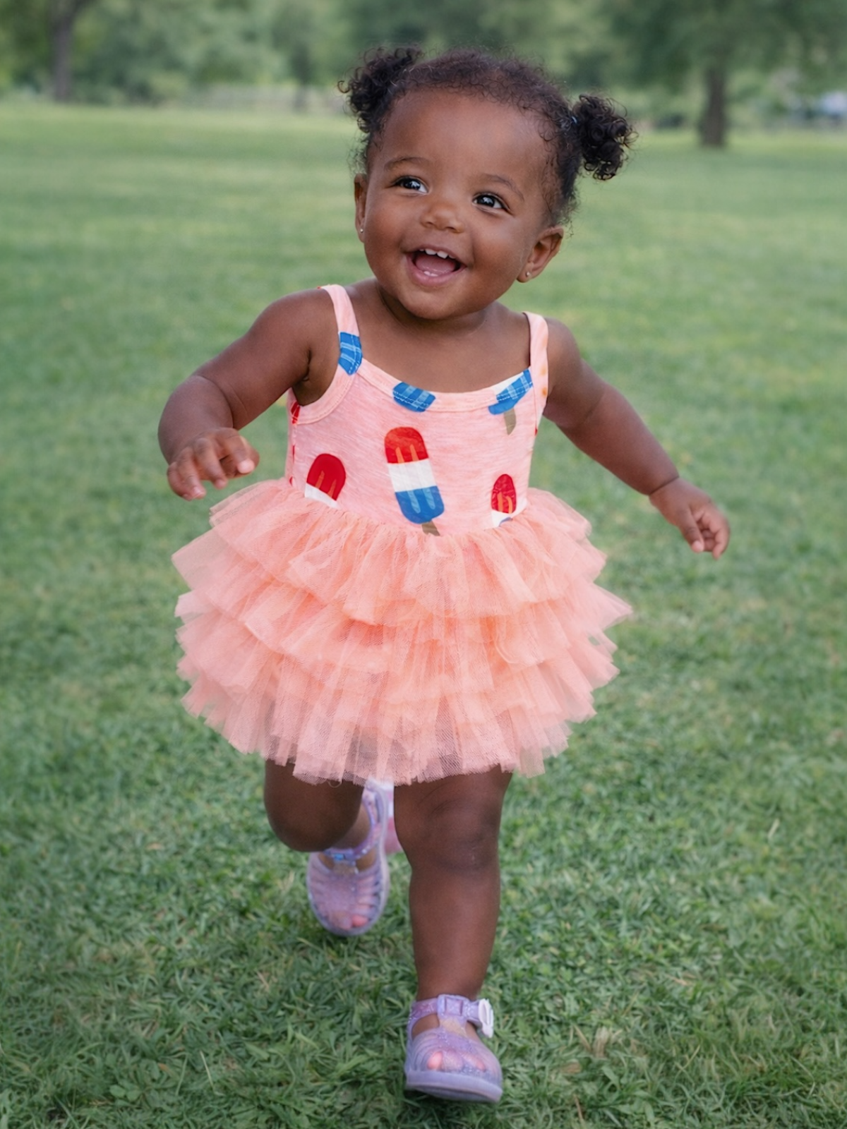 Smiling toddler in a bright dress running on green grass, showcasing joy and playfulness in the outdoors.