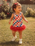 Happy toddler in a star-patterned shirt and red tutu, playing on grassy lawn with flowers and a fence in the background.