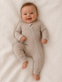 Smiling baby in a beige onesie, lying on a textured white blanket.