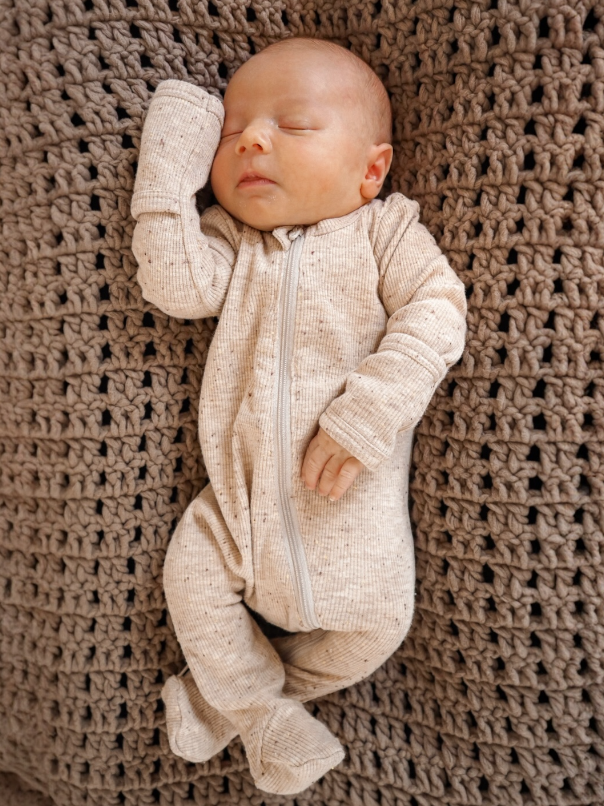 Newborn baby sleeping in a cozy knitted blanket, dressed in a light-colored onesie.