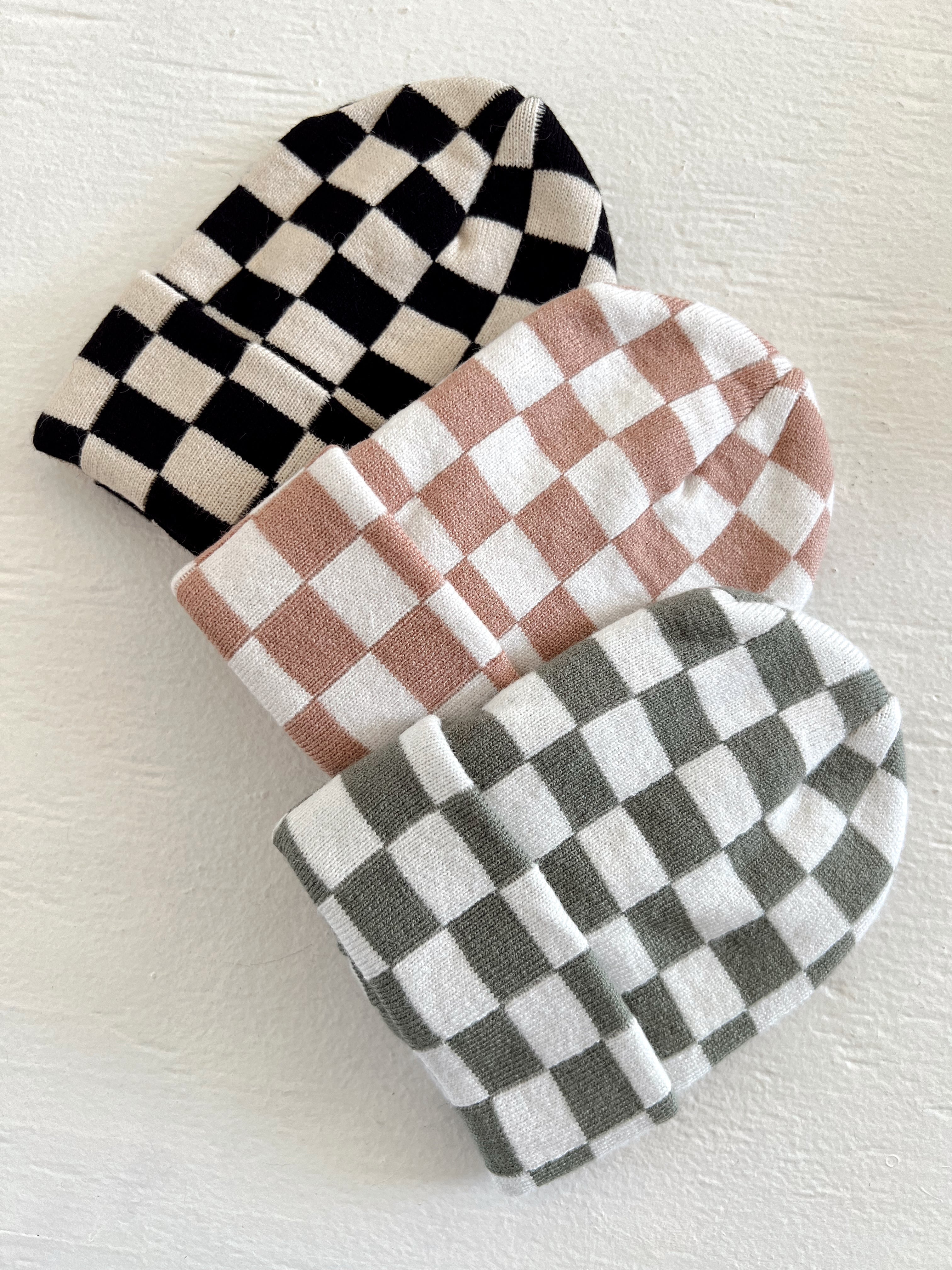 Three checkered beanies in black, pink, and green stacked on a white surface.