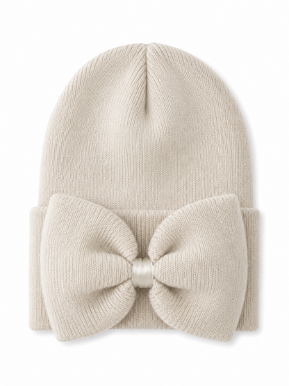 Cream beanie hat with a large bow on the front, perfect for winter fashion.