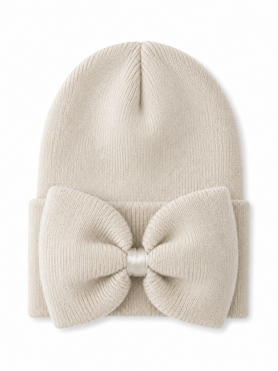 Cream beanie hat with a large bow on the front, perfect for winter fashion.