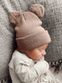 Baby wearing a soft, brown hat with bear ears, sleeping peacefully on a textured gray blanket.