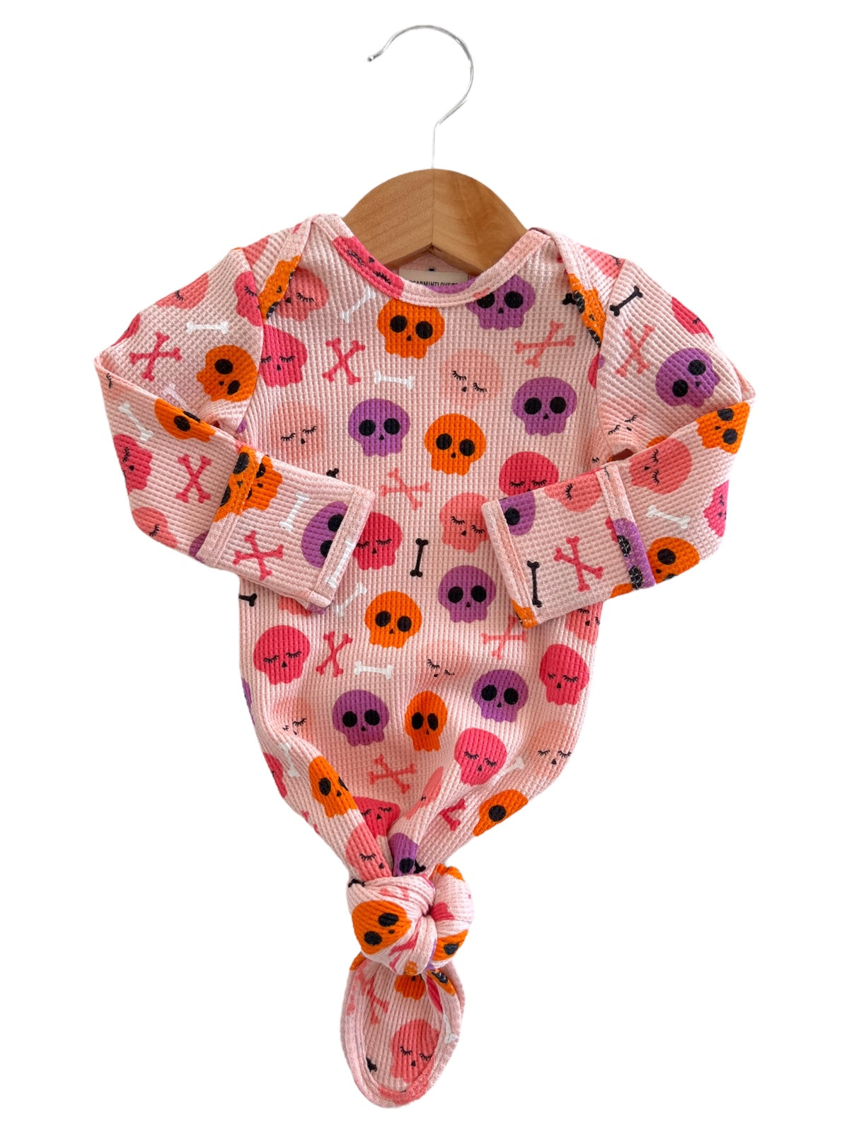 Baby onesie with colorful skull and bone print, hanging on a wooden hanger against a white background.