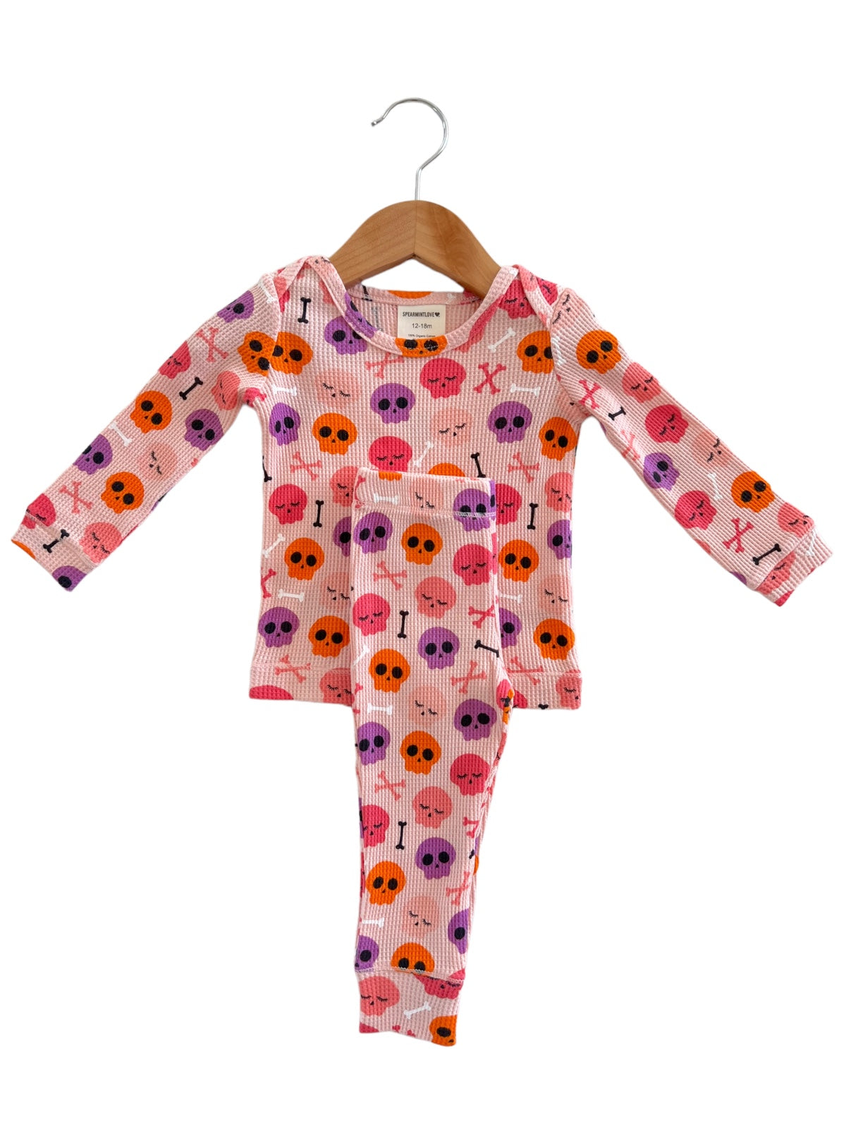 Pink toddler pajamas with colorful skull and bone patterns, hanging on a wooden hanger.
