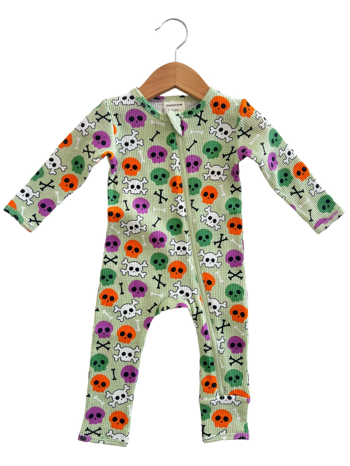 Colorful infant onesie featuring skull and crossbones patterns in orange, green, purple, and black on a light green background.