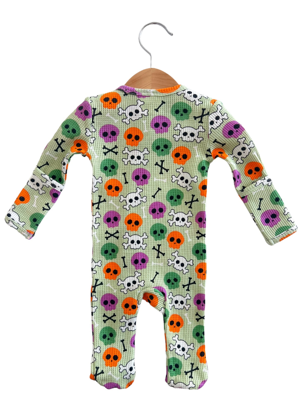 Colorful infant onesie with skull and crossbone pattern in orange, purple, green, and black on a light green background.