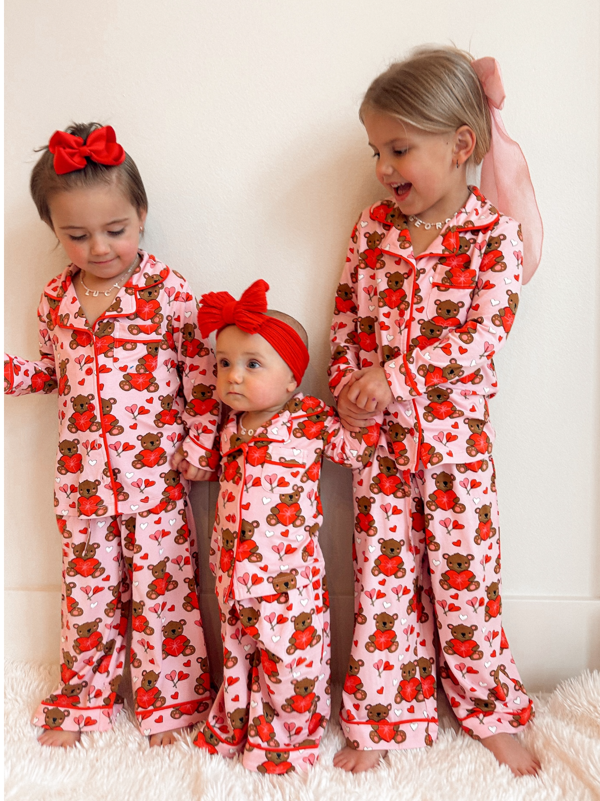 Three girls in matching pink bear print pajamas, smiling and posing against a white background.
