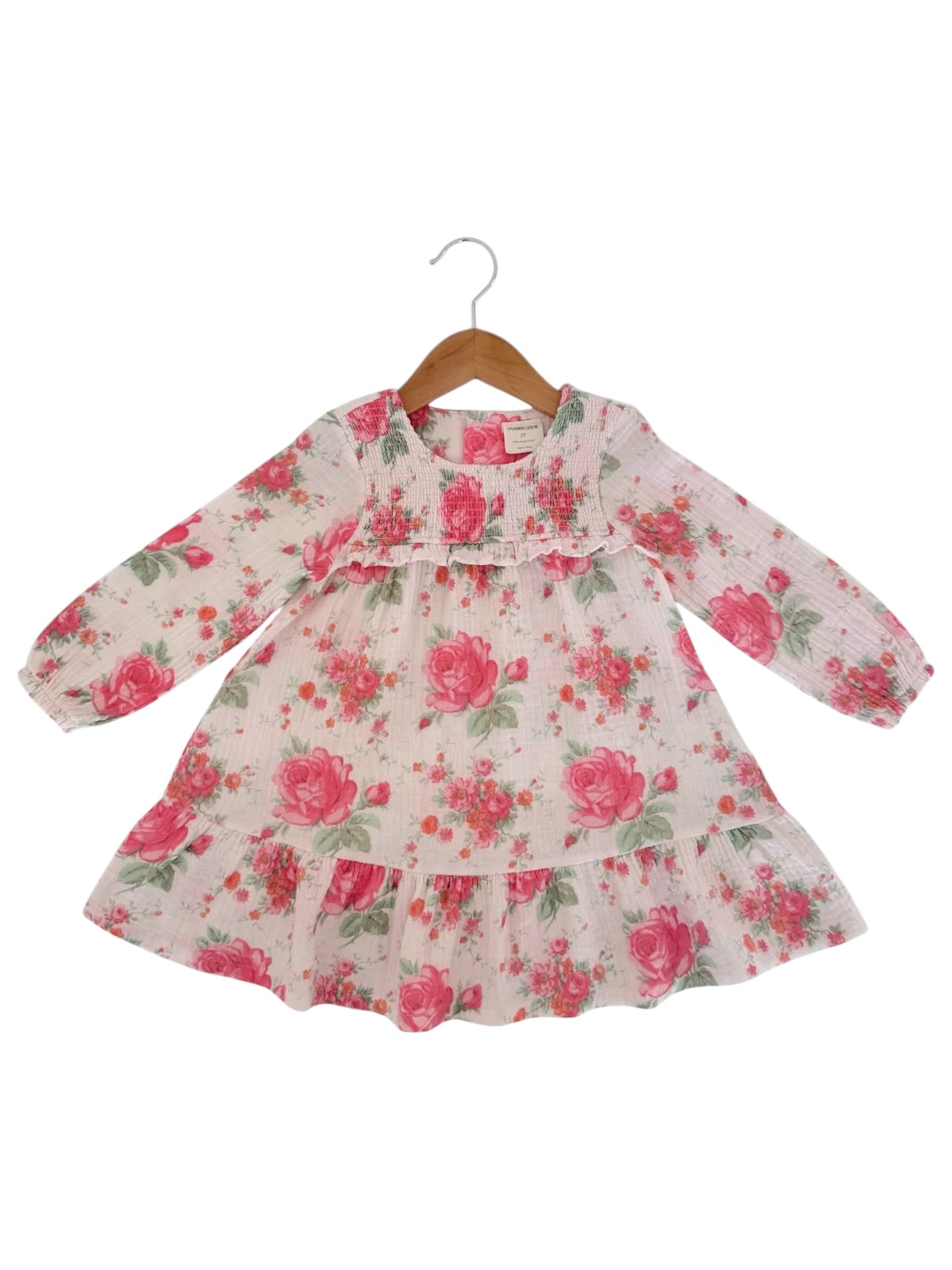White floral dress with pink roses and green leaves, long sleeves, hanging on a wooden hanger.