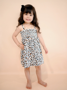 Girl in a leopard print dress poses against a peach background, smiling with a black hair accessory.