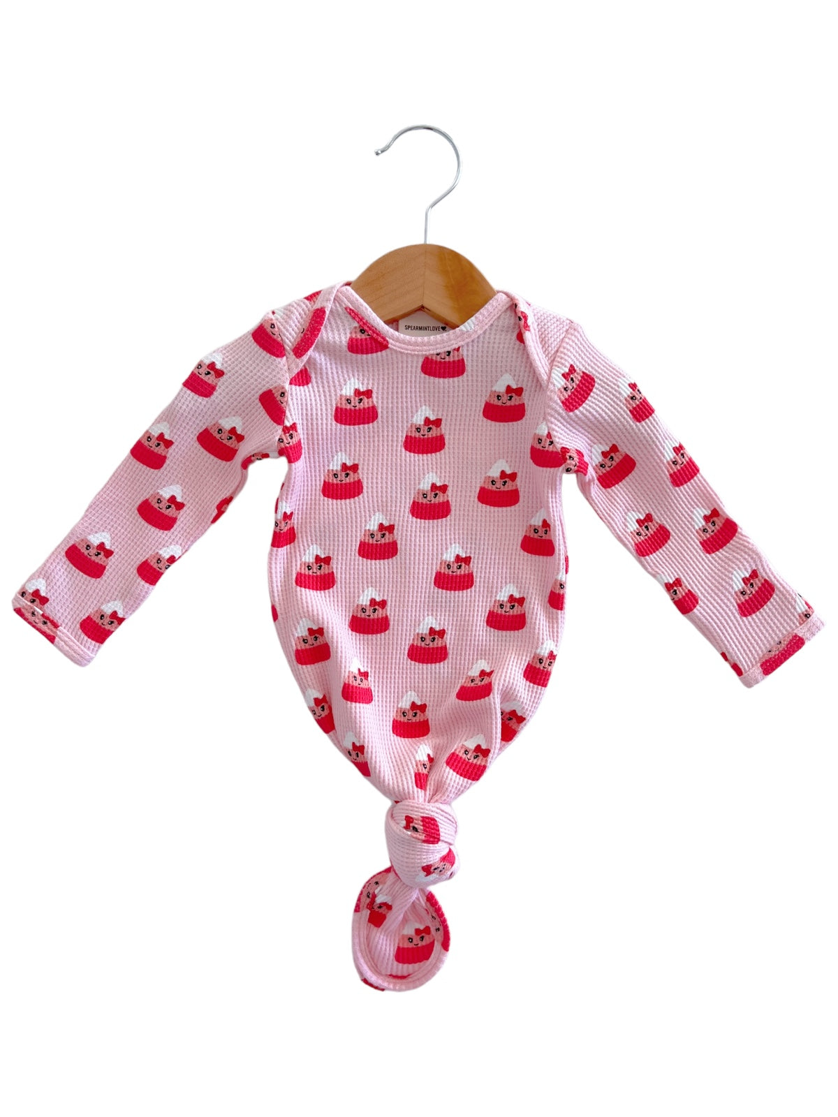 Long-sleeve baby outfit with a pink cupcake pattern, hanging on a wooden hanger.