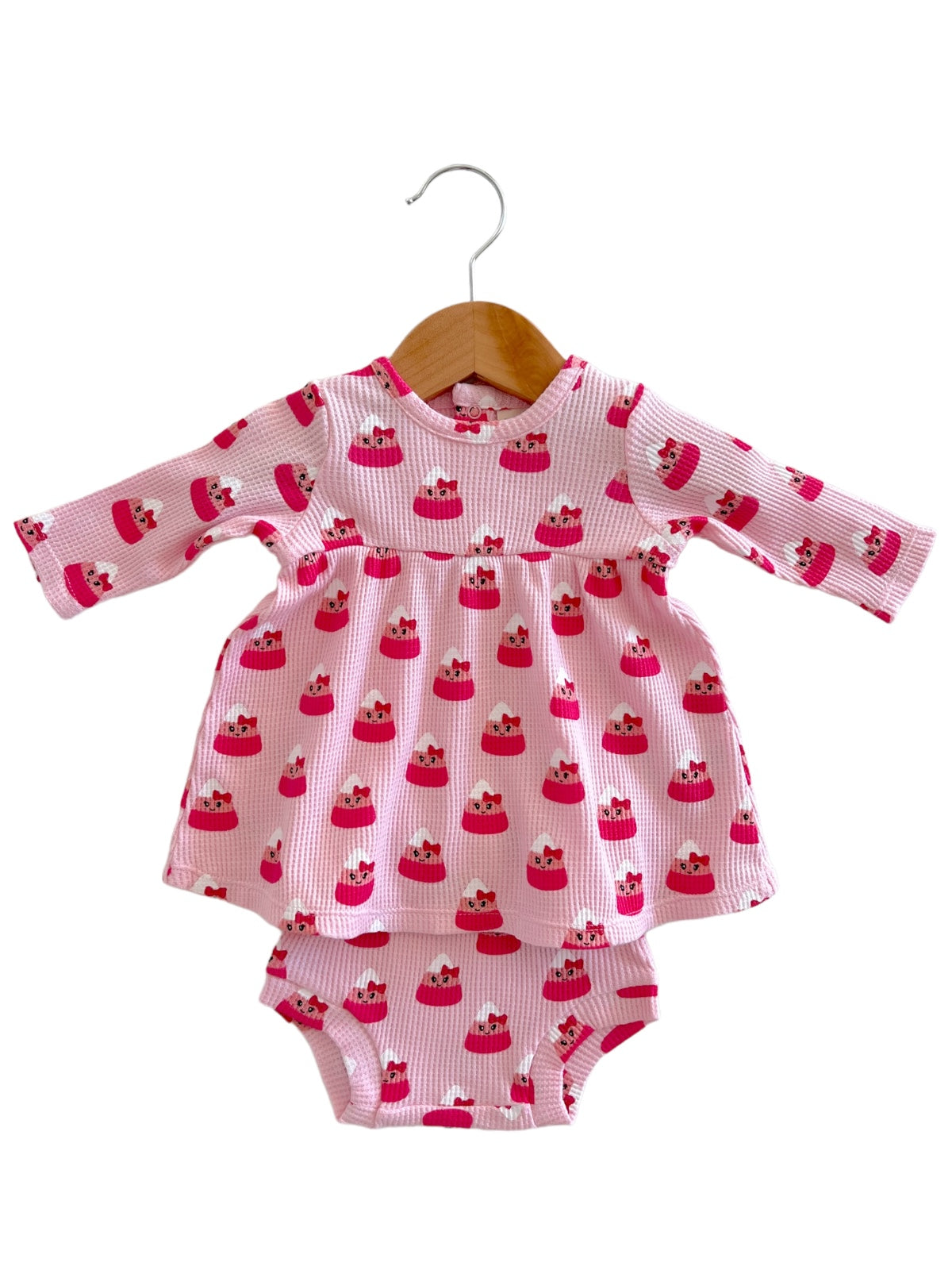 Pink dress with long sleeves featuring a playful cupcake pattern, displayed on a wooden hanger.