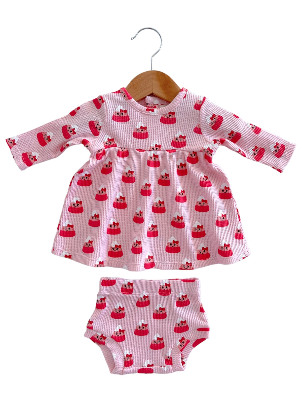Pink dress and bloomer set with a playful cupcake pattern, displayed on a hanger.