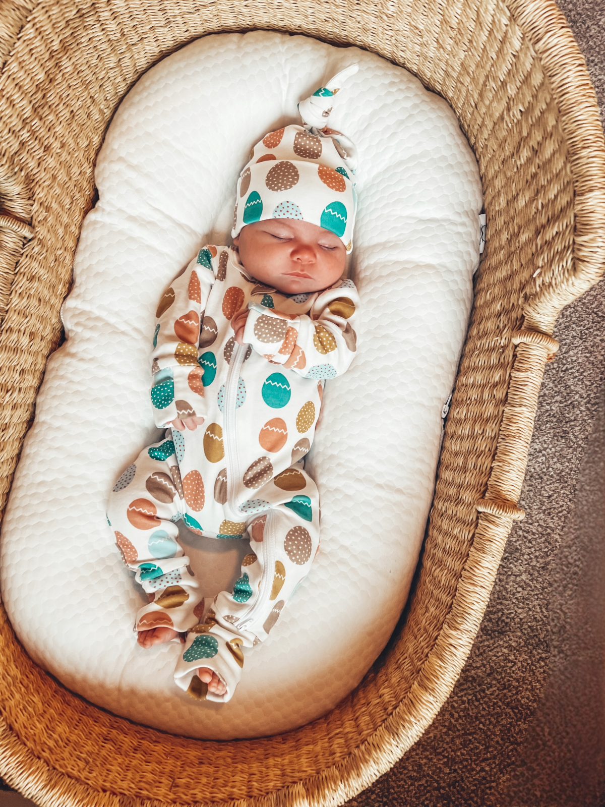 Newborn baby in a patterned onesie and hat, peacefully sleeping in a woven bassinet.