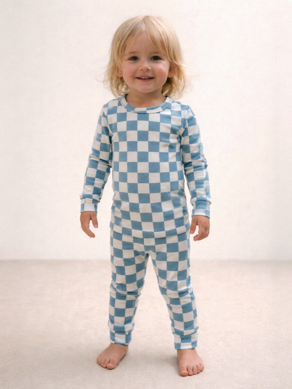 Smiling child in blue and white checkered pajamas standing on a light-colored floor.